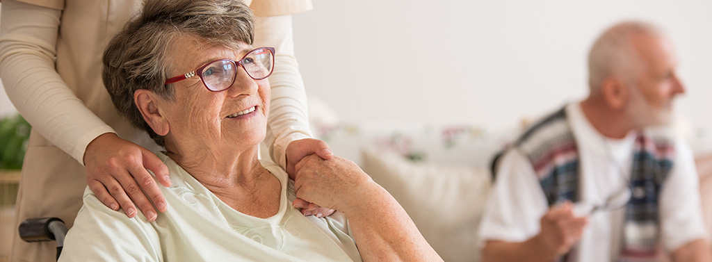 private krankenversicherung ältere frau im rollstuhl mit pflegekraft im hintergrund