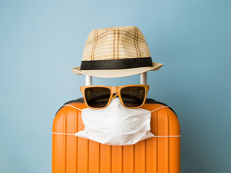 zusatzabsicherung urlaubsreise reisekoffer mit hut sonnenbrille und maske verkleidet