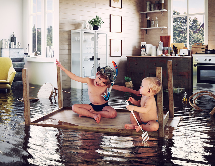 haftpflichtversicherung zwei kinder auf einem tisch als boot in einer ueberschwemmten kueche